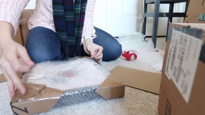 Person verpackt ein gerahmtes Bild sicher in Luftpolsterfolie und Karton.